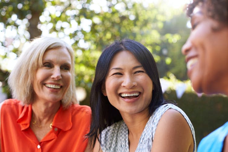 Three women laughing together outdoors.