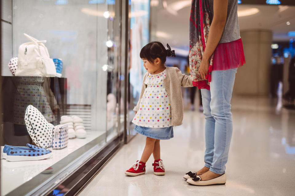 Lovely little girl holding hands with her mom while looking at the shopping window display in the shopping mall joyfully