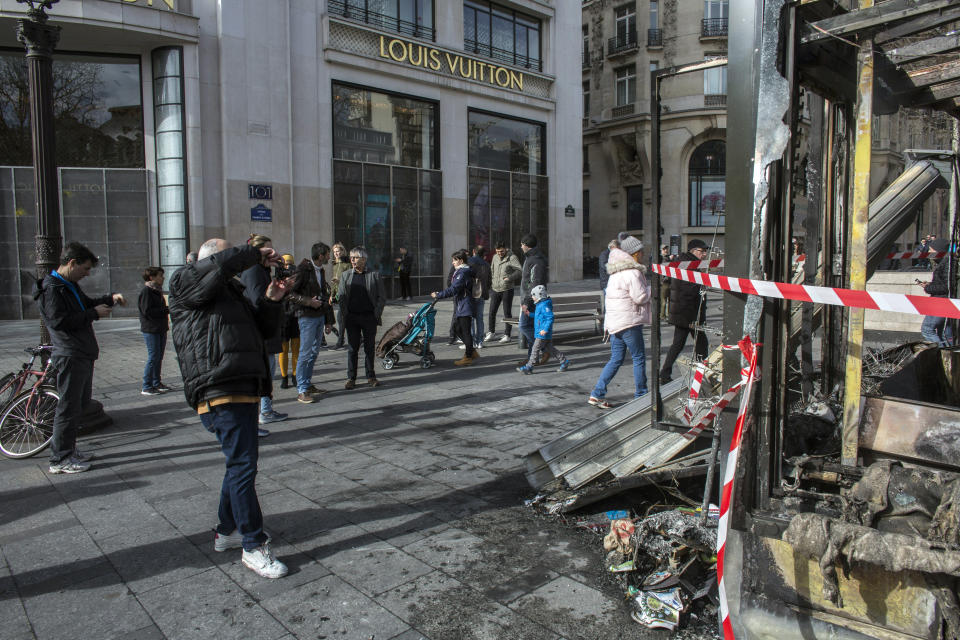 Bystanders take snapshots of the burned out terrasse of the famed restaurant Le Fouquet's on the Champs Elysees the day after it was vandalized and set on fire during the 18th straight weekend of demonstrations by the yellow vests, in Paris, France, Sunday, March 17, 2019. Paris cleaned up one of the world's most glamorous avenues Saturday after resurgent rioting by yellow vest protesters angry at President Emmanuel Macron stunned the nation. (AP Photo/Rafael Yaghobzadeh)