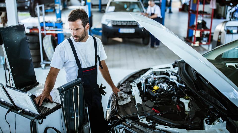 Young mechanic using computer while working on car diagnostics in a repair shop.