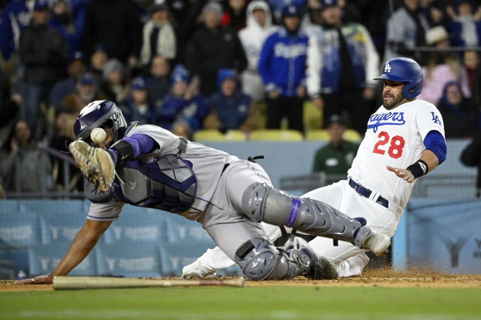 Los Angeles Dodgers' J.D. Martinez, right, scores on a triple by James Outman as Colorado Rockies catcher Elias Diaz dives for a throw that was off target during the fifth inning of a baseball game Monday, April 3, 2023, in Los Angeles. (AP Photo/Mark J. Terrill)