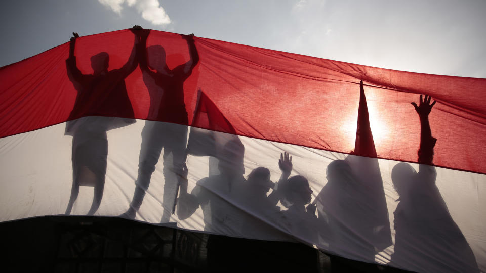 FILE - In this Sept. 26, 2016, file photo, men are silhouetted against a large representation of the Yemeni flag as they attend a ceremony to mark the anniversary of North Yemen's Sept. 26, 1962 revolution in Sanaa, Yemen. President Joe Biden's announcement that the U.S. will end its support of a Saudi-led coalition's years-long war against Yemen's Houthi rebels likely will increase pressure on the kingdom to end its campaign there, though reaching an enduring peace for the Arab world's poorest country still remains in question. (AP Photo/Hani Mohammed, File)