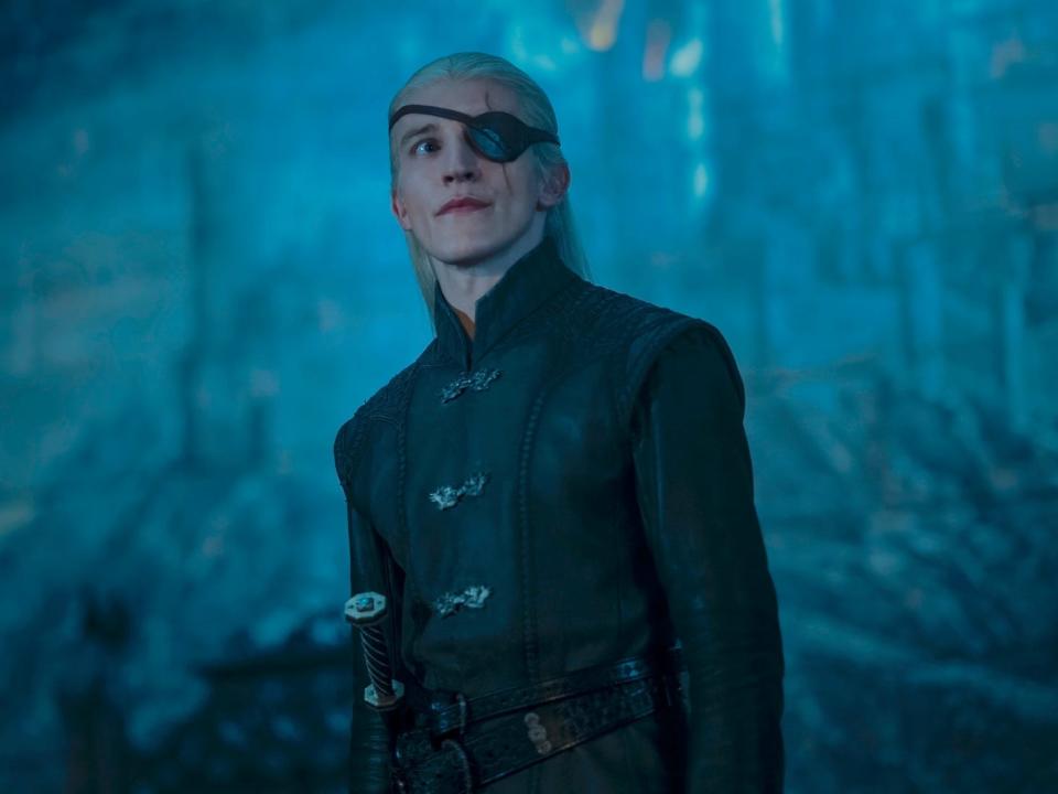 ewan mitchell as aemond targaryen in house of the dragon, wearing a black leather coat and with an eye patch strapped over his eye