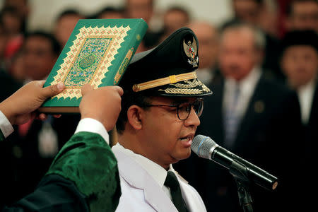 A man holds a Koran as Jakarta Governor Anies Baswedan stands during a swearing-in ceremony at the Presidential Palace in Jakarta, Indonesia, October 16, 2017. REUTERS/Beawiharta