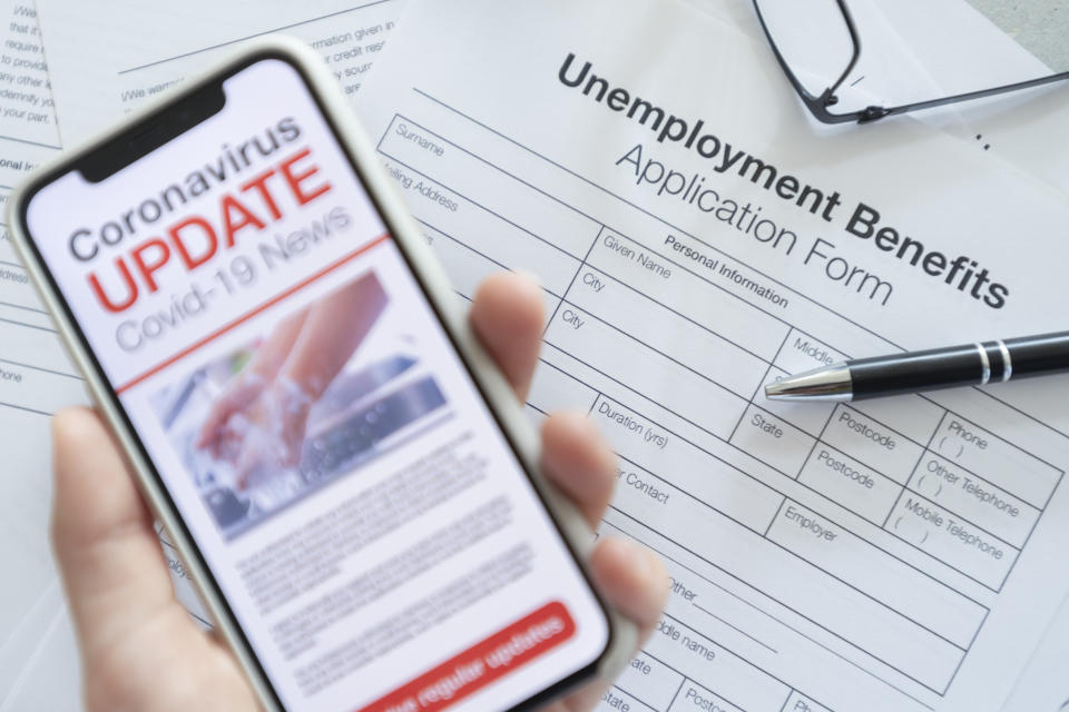 Close up of a mobile phone with Coronavirus covid-19 news update. There is a unemployment benefits application in the background on the desk. The phone is being held and has an image of hand washing hygiene.