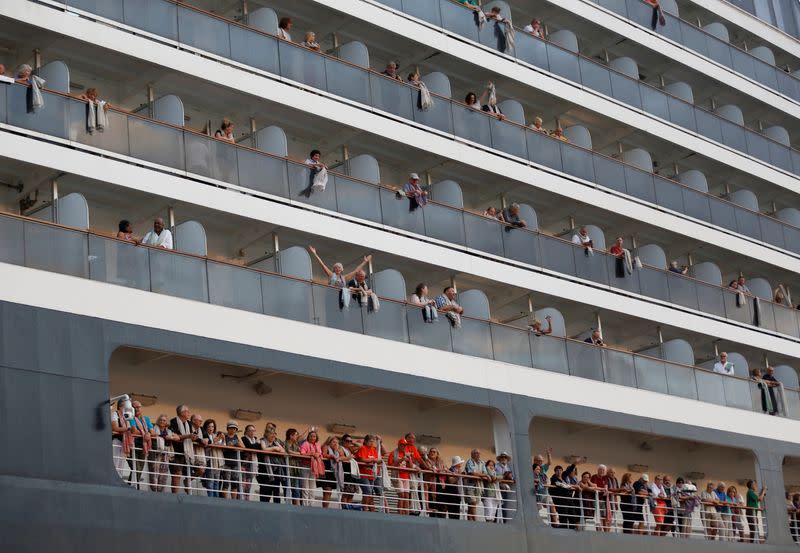 Passengers wave their hands onboard MS Westerdam, a cruise ship that spent two weeks at sea after being turned away by five countries over fears that someone aboard might have the coronavirus, as it docks in Sihanoukville