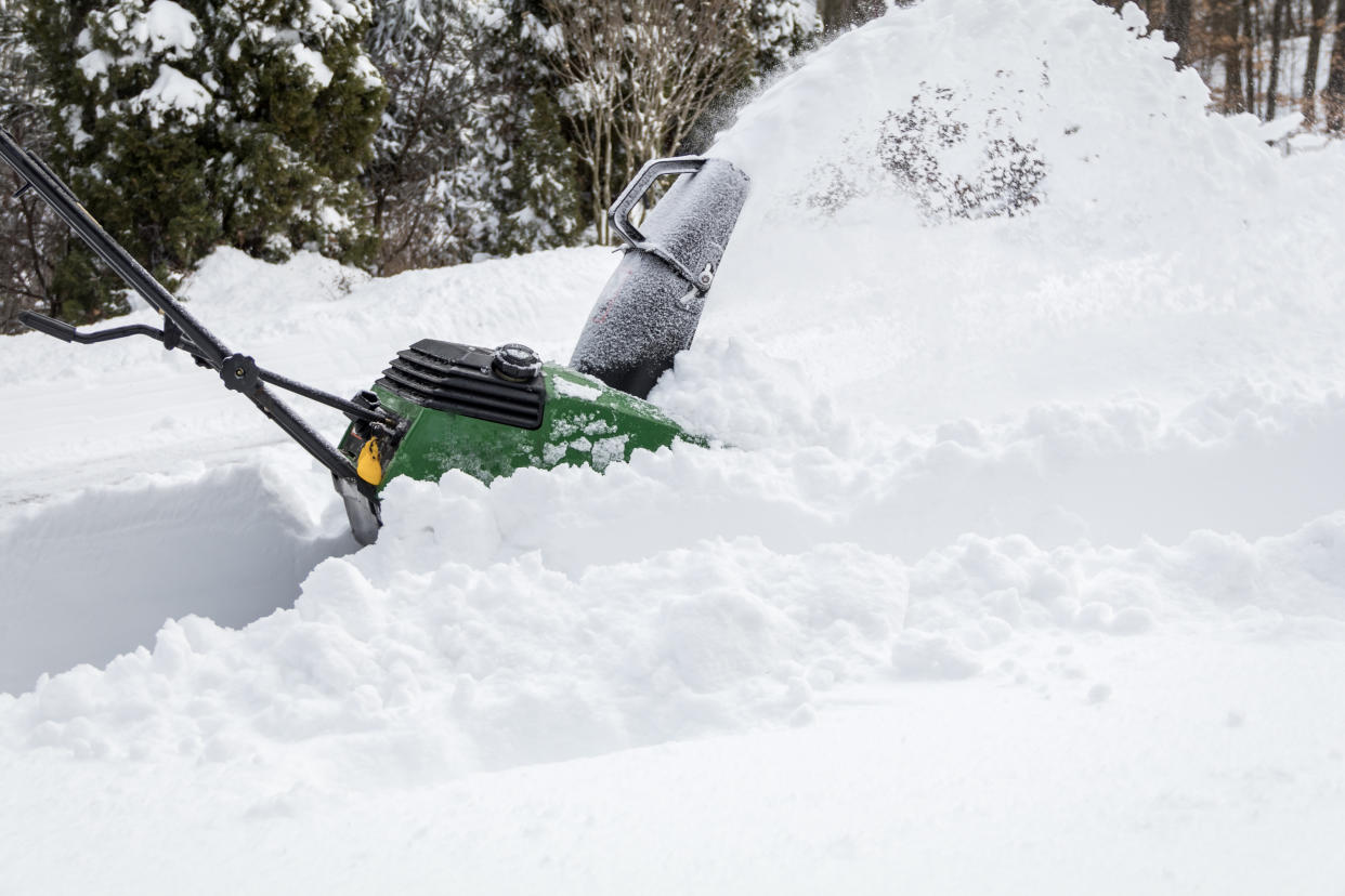 Snow blower in action clearing a residential driveway after snow storm.  Snow removal, winter snow storm, weather concept.