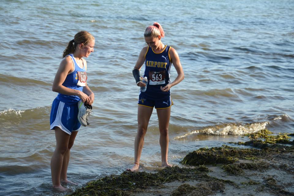 Race winner Jenna Pilachowski of Jefferson (left) and runner-up Cecilia Ortega of Airport cool their feet off in Lake Erie after the Huron League cross country jamboree at Sterling State Park. Ortega was running with a cast on her broken arm.