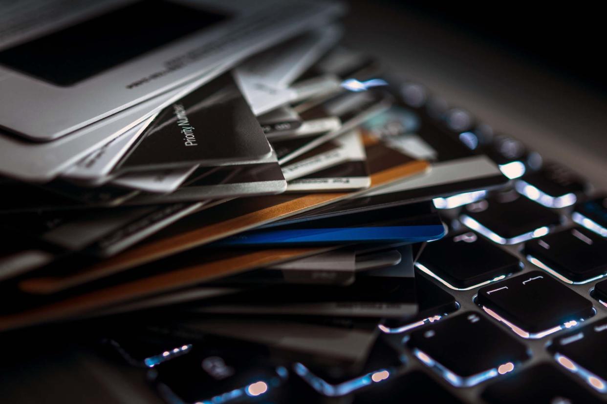 Closeup of a large stack of credit cards on a lite-up black keyboard of a laptop, dark shadowing, blurred around the edges