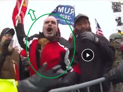 A screenshot of a video shows a crowd of Trump supporters pushing up against a police barricade, including one man who appears to be shouting and is holding a flag pole above his head.
