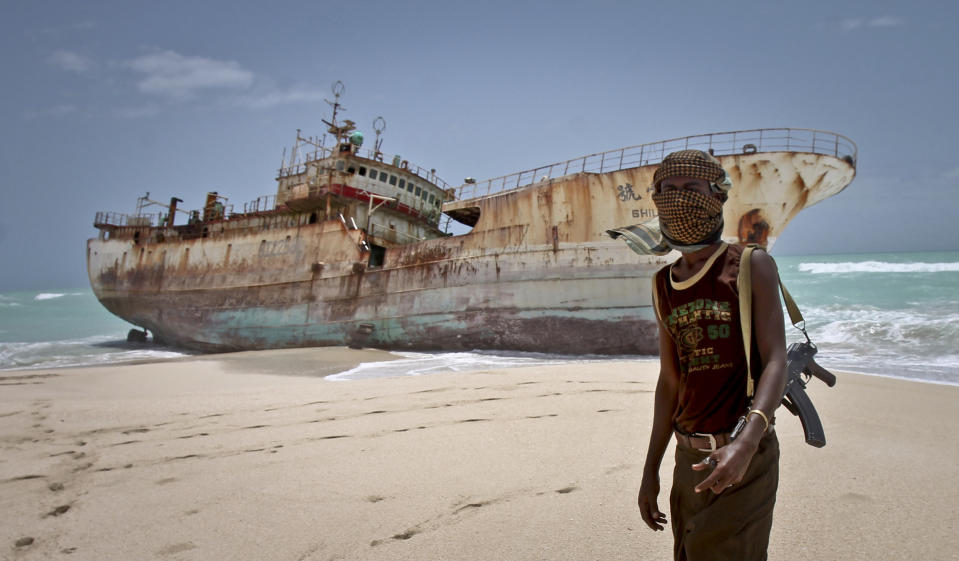 In this photo taken Sunday, Sept. 23, 2012, masked Somali pirate Abdi Ali stands near a Taiwanese fishing vessel that washed up on shore after the pirates were paid a ransom and released the crew, in the once-bustling pirate den of Hobyo, Somalia. The empty whisky bottles and overturned, sand-filled skiffs that litter this shoreline are signs that the heyday of Somali piracy may be over - most of the prostitutes are gone, the luxury cars repossessed, and pirates talk more about catching lobsters than seizing cargo ships. (AP Photo/Farah Abdi Warsameh)