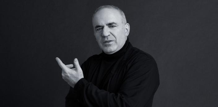 Black-and-white image of Garry Kasparov in a dark turtleneck sweater appearing to pose with his left hand slightly pointing up.