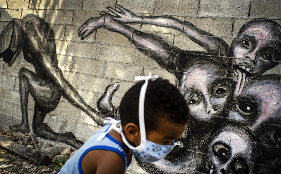 A boy wearing a mask as a precaution against the spread of the new coronavirus plays in front of a mural by artist Yulier P. titled "Marcha Hacia la Oscuridad," or Move Toward Darkness, in the patio of a home in Havana, Cuba, Friday, April 10, 2020. Yulier P. said his latest murals show humanity's powerlessness against the COVID-19 disease. (AP Photo/Ramon Espinosa)