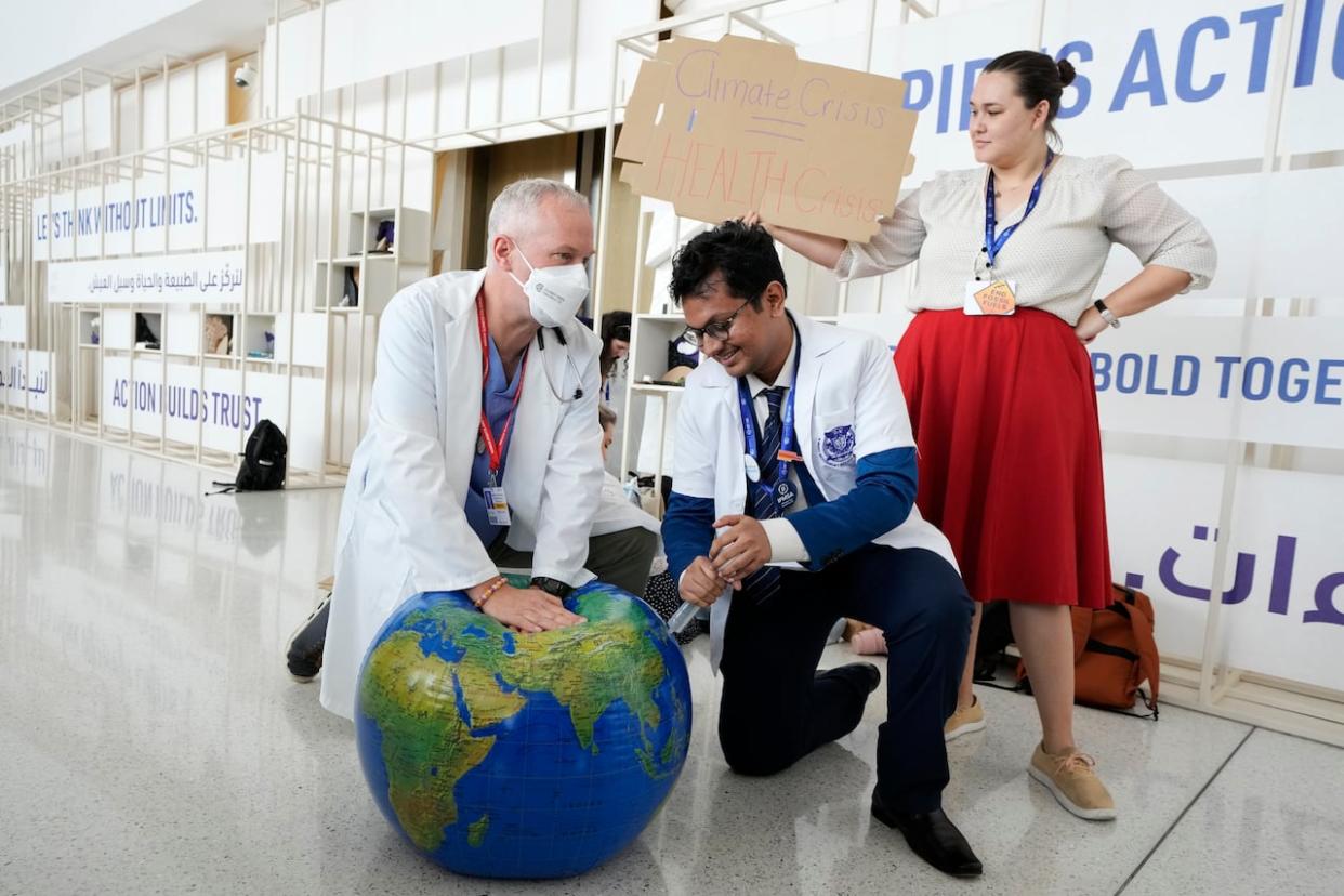 Joseph Vipond, left, of the Canadian Association of Physicians for the Environment, pretends to resuscitate the Earth during a demonstration at the COP28 UN climate summit on Sunday in Dubai, United Arab Emirates. (Peter Dejong/The Associated Press - image credit)