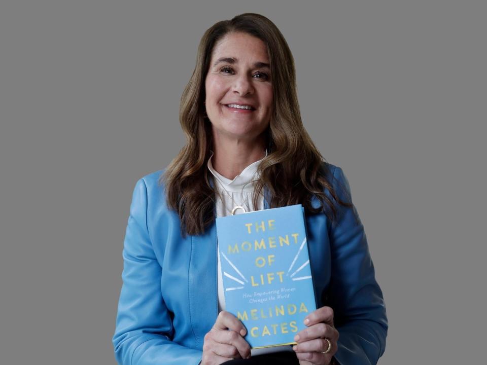 Melinda Gates poses with her  book, "The Moment of Lift," graphic element on gray