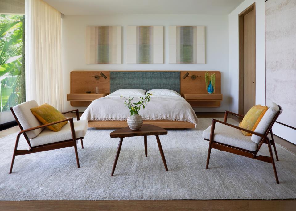 In the primary bedroom, Sandra Weingort custom-designed the bed and nightstands. The linens are from Kassatex and the rug was sourced from Beauvais Carpets. Two 1960s lounge chairs by Ib Kofod-Larsen pair nicely with a coffee table by Mira Nakashima on which a vase from Côte À Coast was placed. Apparatus Studio designed the sconces while the triptych is by Myles Bennett.