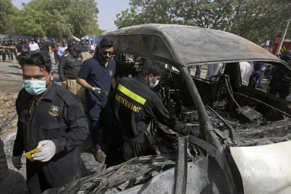 Pakistani investigators examine a burned van at the site of explosion in Karachi, Pakistan, Tuesday, April 26, 2022. The explosion ripped through a van inside a university campus in southern Pakistan on Tuesday, killing several people including Chinese nationals and their Pakistani driver, officials said. (AP Photo/Fareed Khan)