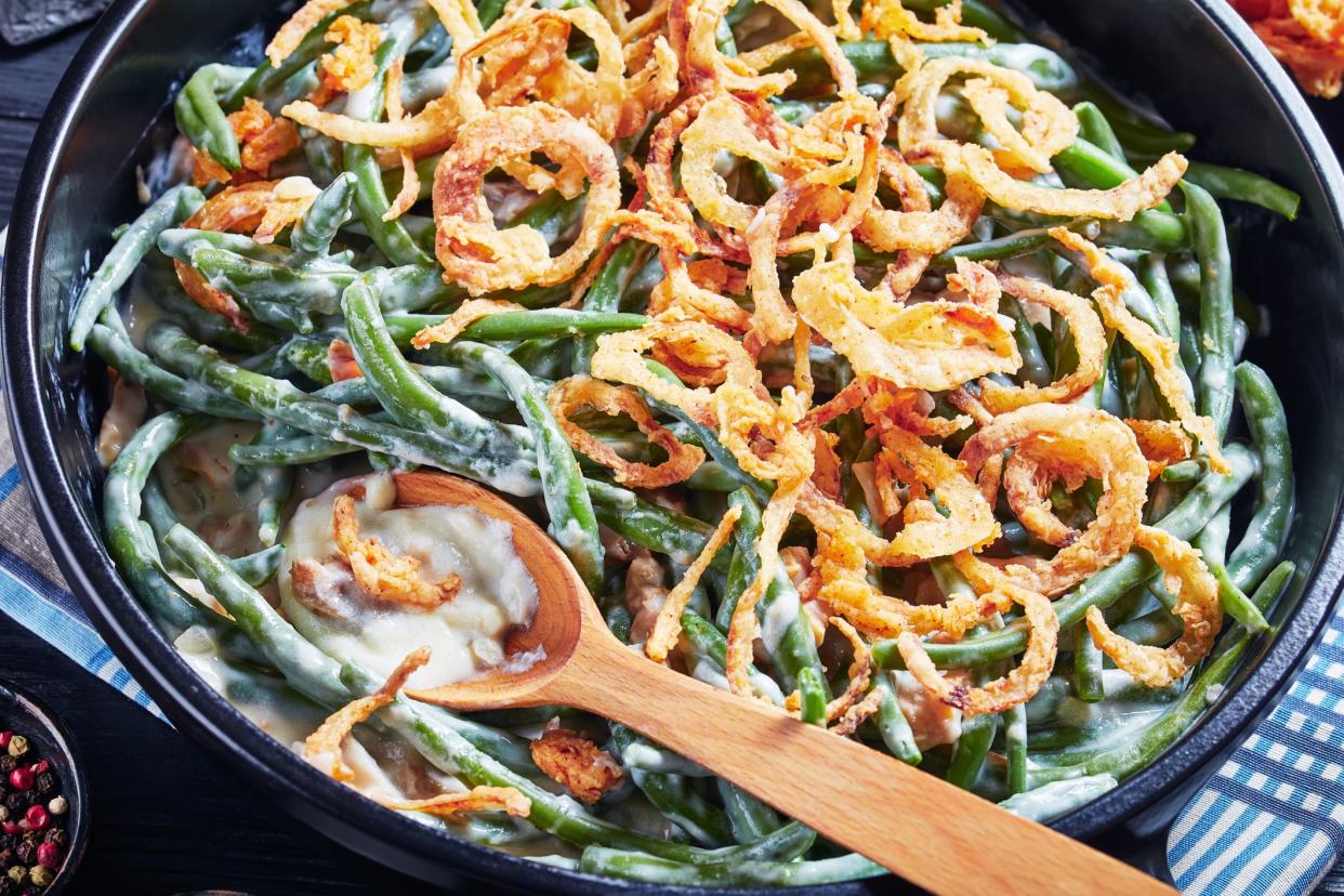 close-up of Green Bean Casserole topped with crispy fried onions in a black dish with spoon,  american cuisine, view from above