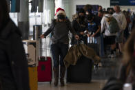 FILE - Donning a Santa Claus hat, Caitlin Banford waits in line to check in for her flight to Washington at Los Angeles International Airport in Los Angeles, Dec. 20, 2021. For the second year in a row, the ever-morphing coronavirus presents would-be holiday revelers with a difficult choice: cancel their trips and celebrations yet again or figure out how to forge ahead as safely as possible. Many health experts are begging people not to let down their guard, but pandemic fatigue is real. While travel restrictions in some places have forced cancellations, many governments have been reluctant to order more lockdowns. (AP Photo/Jae C. Hong)