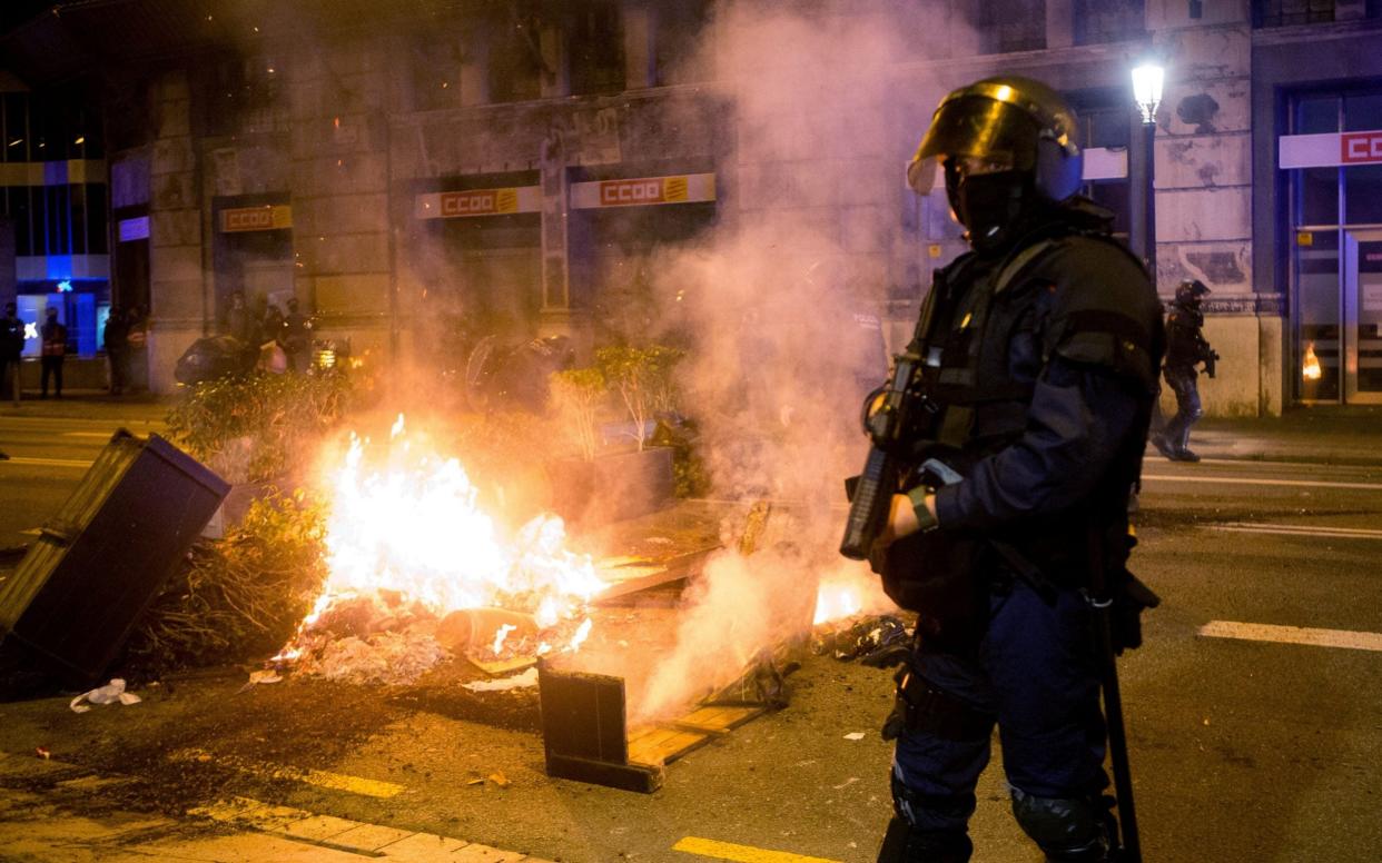 Mossos d'Esquadra agents stand guard as COVID-19 deniers burn urban furniture during a march to protest - Shutterstock