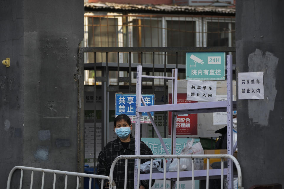 FILE - A woman wearing a face mask looks out from the barriers set up in a locked down neighborhood as part of COVID-19 controls in Beijing, Wednesday, Nov. 23, 2022. (AP Photo/Andy Wong, File)