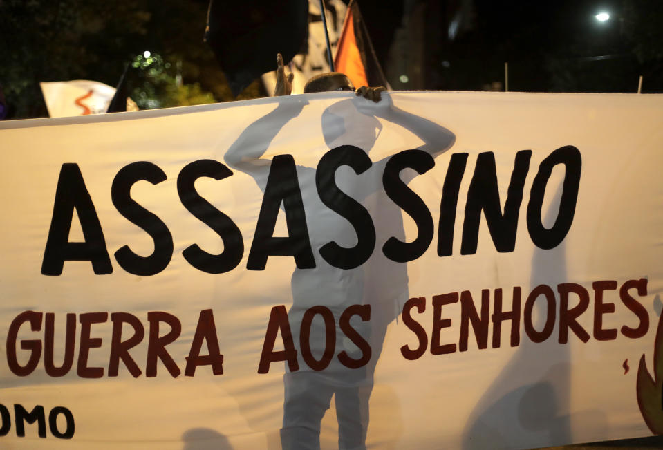 FILE - A demonstrator stands behind a banner that reads in Portuguese "Assassin," in reference to Brazilian President Jair Bolsonaro, during a protest calling for the resignation of Bolsonaro, who is fighting corruption charges in Senate hearings investigating the purchase of vaccines to fight the COVID-19 pandemic, in Rio de Janeiro, Brazil, Tuesday, July 13, 2021. Democracy is deteriorating across the world, with countries notably taking undemocratic and unnecessary actions to contain the coronavirus pandemic, an intergovernmental body, the International Institute for Democracy and Electoral Assistance, or International IDEA, said in its new report Monday, Nov. 22, 2021. (AP Photo/Bruna Prado, File)