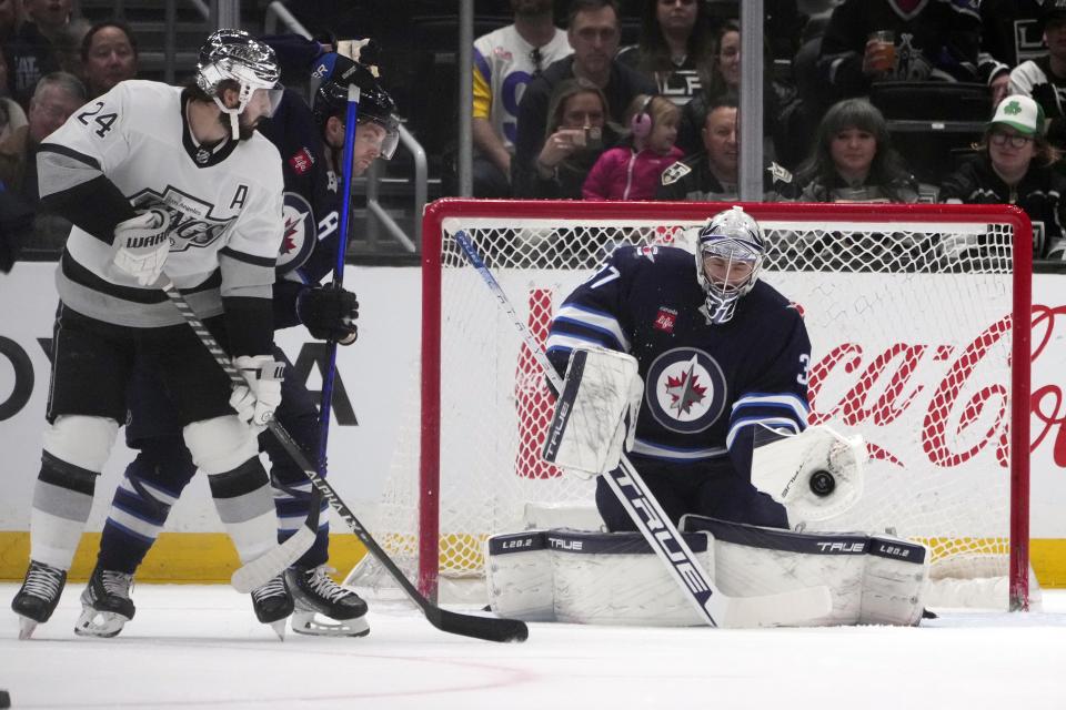 Winnipeg Jets goaltender Connor Hellebuyck, right, stops a shot during the first period of an NHL hockey game against the Los Angeles Kings Saturday, March 25, 2023, in Los Angeles. (AP Photo/Marcio Jose Sanchez)