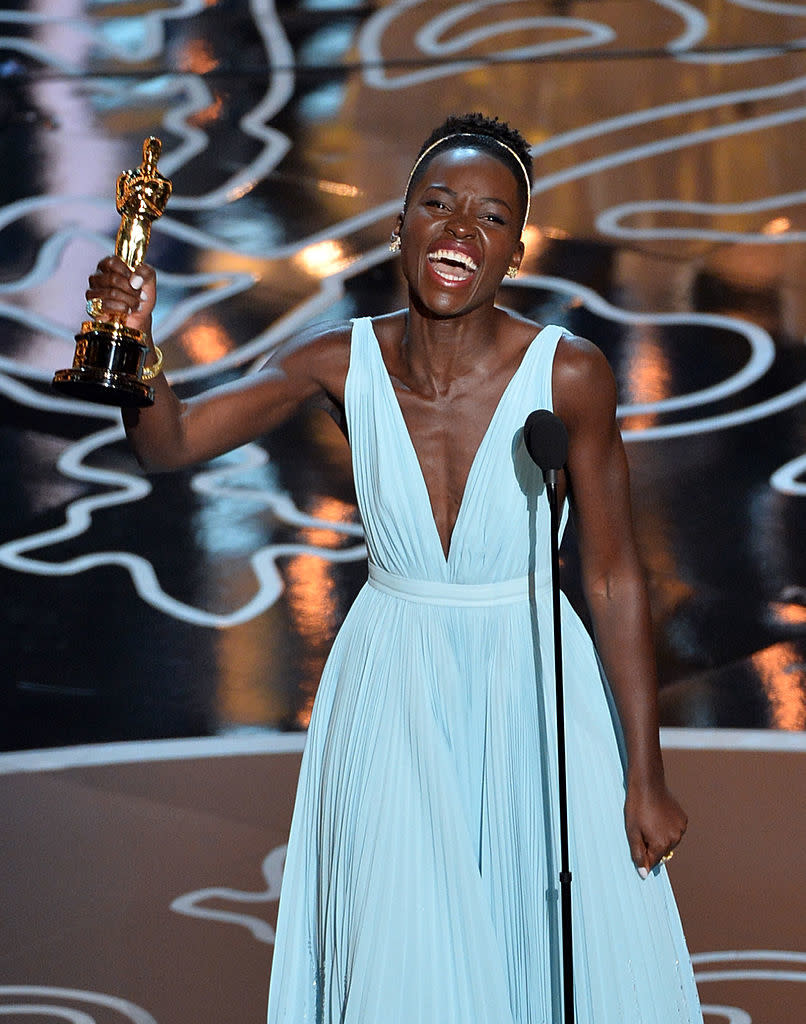 Lupita Nyong'o in a v-neck gown, joyfully holding an Oscar at the award ceremony