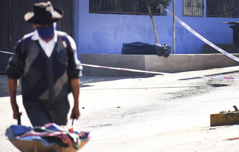 Un hombre empuja una carretilla mientras al fondo se observa el cadáver de un hombre envuelto en una bolsa de plástico en una calle de Cochabamba, Bolivia, el domingo 5 de julio de 2020. Según un pariente, el hombre murió el sábado con aparentes síntomas de COVID-19 mientras salía de su casa a buscar un doctor (Foto AP/Dico Solís)