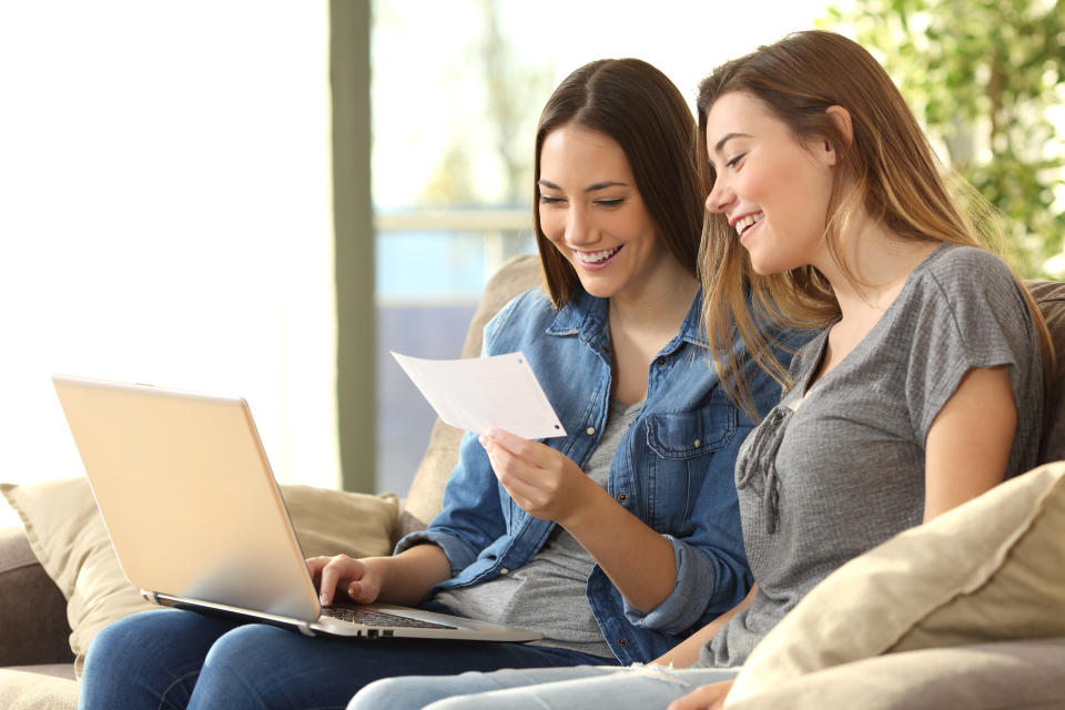 Two roommates checking bank mails on line with a laptop sitting on a couch in the living room at home