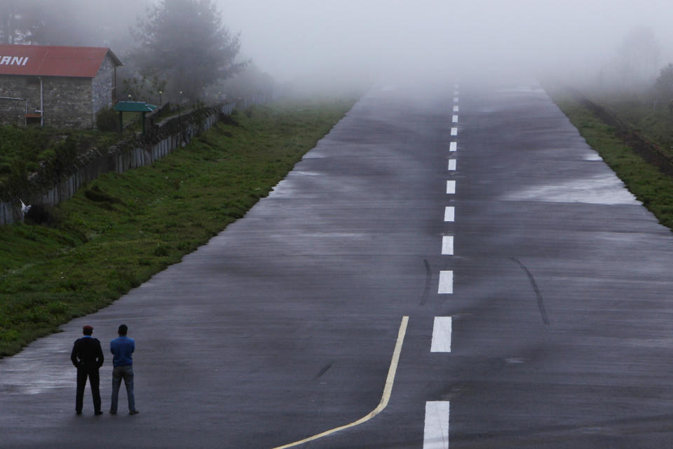 In this Sunday, May 26, 2013 photo, policemen stand on the runway during bad weather conditions at Lukla airport, Nepal. Carved out of side of a mountain, the airport was built by Sir Edmund Hillary in 1965, and at an altitude of 2,843 meters (9,325 feet) it has earned the reputation of being one of the most extreme and dangerous airports in the world. (AP Photo/Niranjan Shrestha)