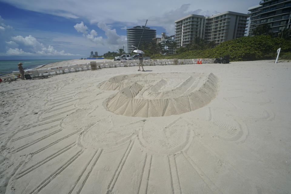 A giant heart sculpted from sand adorns the beach beside the area that is closed for search and rescue operations at the partially collapsed Champlain Towers South condo building, Friday, July 2, 2021, in Surfside, Fla. A crane works at the Champlain Towers South site in the distance, while Champlain Towers North is seen at right, and Champlain Towers East is seen center right. (AP Photo/Gerald Herbert)