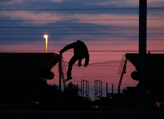 A migrant climbs over a fence on to the tracks at the Eurotunnel site at Coquelles in Calais