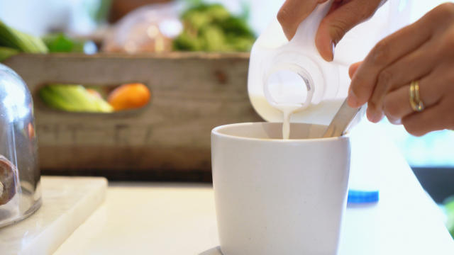 A woman pours milk in her coffee.