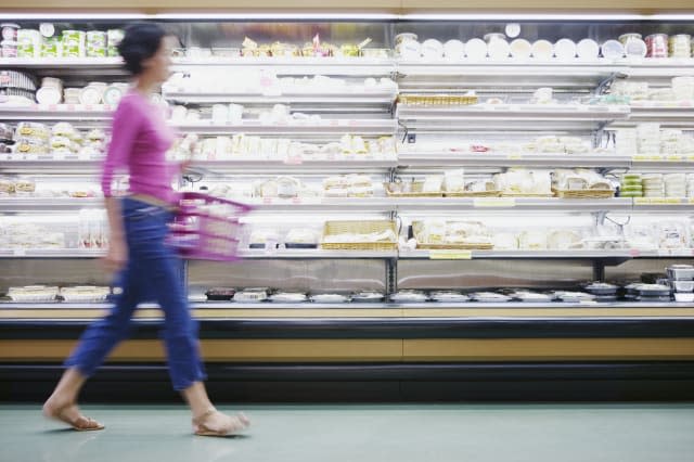 Young woman holding a shopping basket walking past isles in a supermarket (blurred)