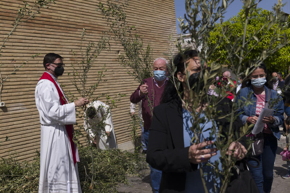 A Catholic priest distributes palms among worshipers prior to a Palm Sunday mass during the Holy Week, outside Nuestra Senora de la Candelaria church in Seville, southern Spain, Sunday, March 28, 2021. Few Catholics in devout southern Spain would have imagined an April without the pomp and ceremony of Holy Week processions. With the coronavirus pandemic unremitting, they will miss them for a second year. (AP Photo/Laura Leon)