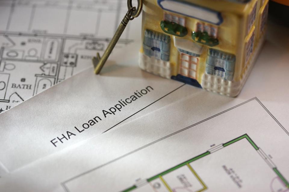 A close up of a document entitled 'FHA loan application' under a yellow toy house and a brass key.