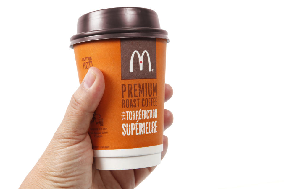 McDonalds coffee cup (McCafe) in a hand on a white background. McDonalds is the world\'s largest chain of hamburger fast food restaurants.