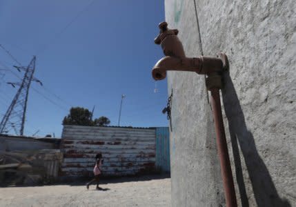 FILE PHOTO: Residents walk past a leaking communal tap in Khayelitsha township, near Cape Town, South Africa, December 12, 2017. Picture taken December 12, 2017. REUTERS/Mike Hutchings