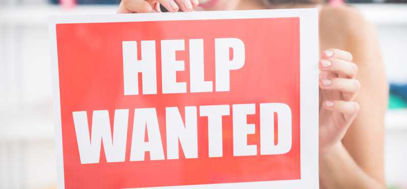 woman hanging help wanted sign in window