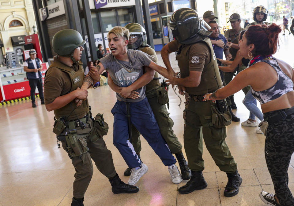 FILE - In this March 20, 2020 file photo, police detain two street vendors to evict them from the train station in Santiago, Chile, after the government ordered businesses to close and street vendors to go home as a precaution against the spread of the new coronavirus. Many of the wealthy are already recovering from coronavirus and experts are warning that the virus could kill untold numbers in the poorest sectors of society, where not working means not eating. (AP Photo/Esteban Felix, File)