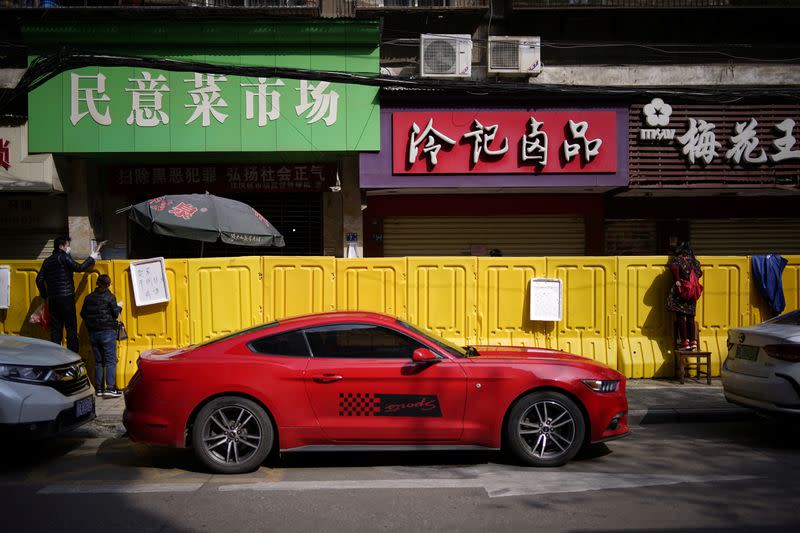 Residents pay for groceries by standing on chairs to peer over barriers set up to ring fence a wet market on a street in Wuhan