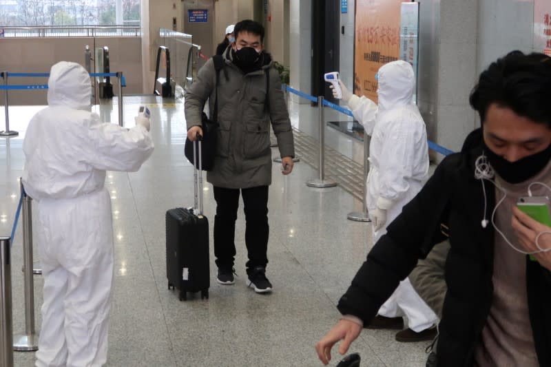 Workers in protective suits check the temperature of a passenger arriving at the Xianning North Station on the eve of the Chinese Lunar New Year celebrations, in Xianning