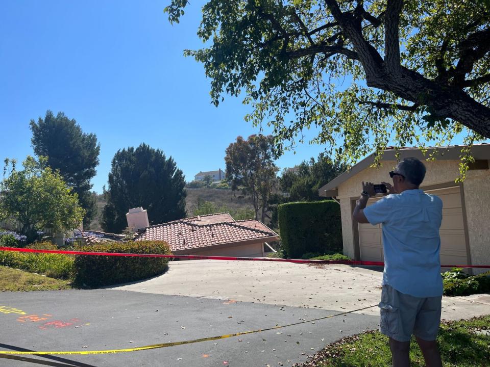 A person photographs a house that appears to be sinking on one side.