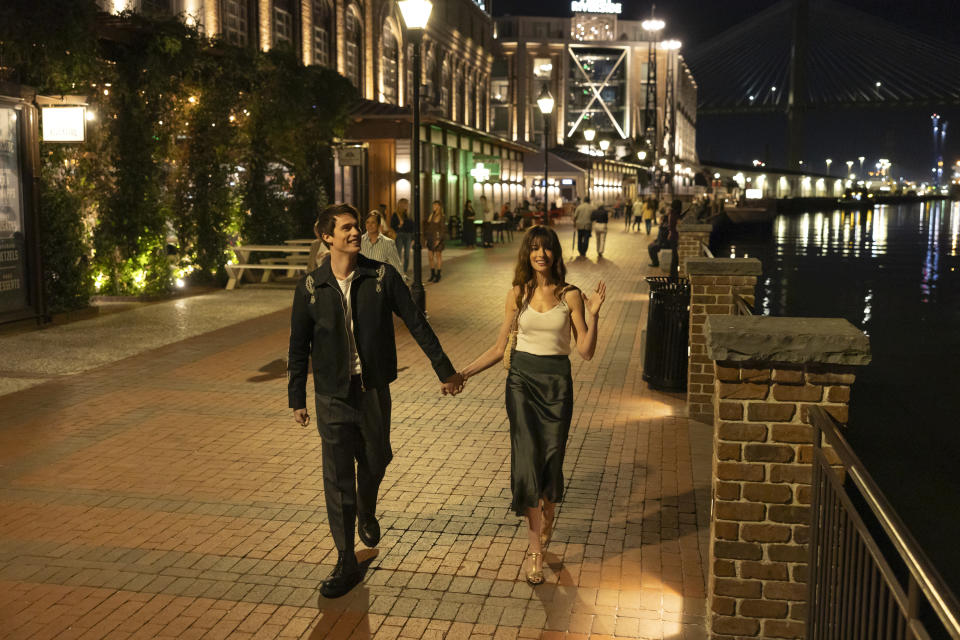 Two characters from a TV show or movie walking hand in hand on a waterfront promenade at night