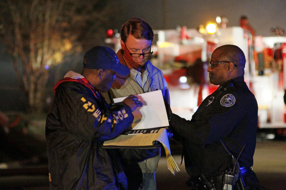 Investigators review notes as fire fighters combat a fire in a west Jackson, Miss., home where authorities say a small plane carrying three people crashed shortly after 5 p.m. Tuesday evening, Nov. 13, 2012. The home's resident is believed to have escaped but authorities have not released names of plane's passengers. (AP Photo/Rogelio V. Solis)