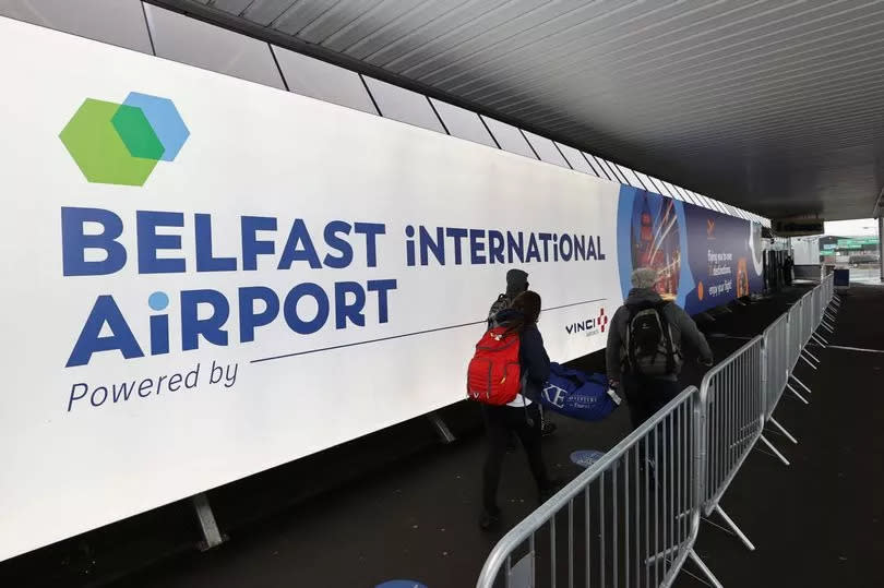 Passengers with luggage walking past a Belfast International Airport sign outside the airport