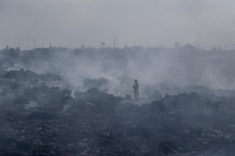 FILE - In this Tuesday, Sept. 7, 2021 file photo, a man who scavenges recyclable materials for a living walks across a mountain of garage amidst smoke from burning trash at Dandora, the largest garbage dump in the capital Nairobi, Kenya. The World Health Organization said Wednesday Sept. 22, 2021, the negative health impacts of poor air quality kick in at lower levels than it previously thought, announcing revisions to its guidelines on air quality that set a higher bar for policymakers in a world where 90 percent of people already live in areas with one particularly harmful type of pollutant. (AP Photo/Brian Inganga, File)