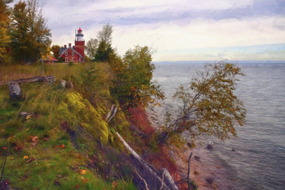 A quaint lighthouse nestled on a grassy cliff overlooks a calm body of water. Trees and bushes line the cliff's edge. The sky is partly cloudy