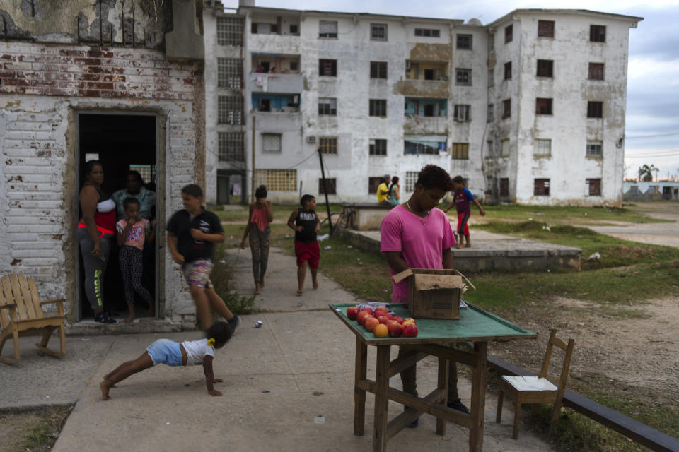 An apple vendor stands amid playing children in La Coloma, Pinar del Rio province, Cuba, Wednesday, Oct. 5, 2022, a week after Hurricane Ian. (AP Photo/Ramon Espinosa)